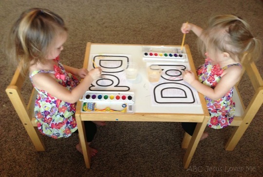 Twin girls sitting at a table painting.
