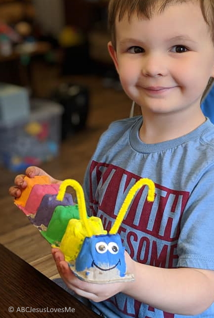 Little boy holding a painted egg-carton carterpillar.