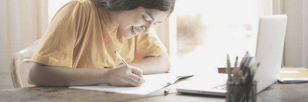 Woman writing while looking at Zoom on the laptop