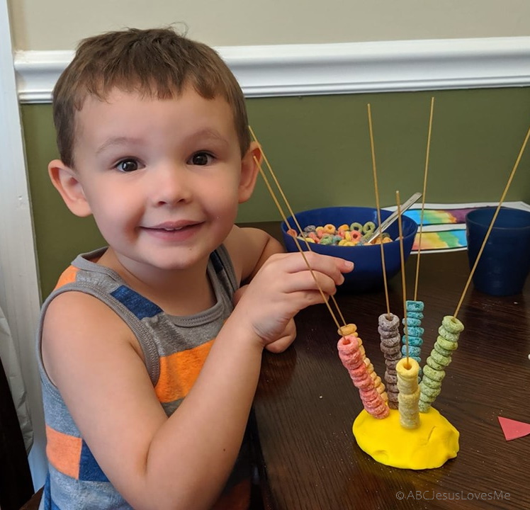 Little boy threading Froot Loops on spaghetti noodles.